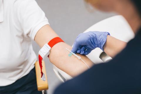 Detail Blutabnahme in medizinischer Praxis: Pflegekraft mit Handschuhen und Spritze bei Blutabnahme an Patientenarm.